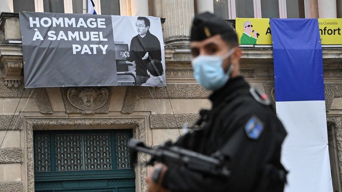 A French police officer stands next to a portrait of French teacher Samuel Paty on display on the facade of the Opera Comedie in Montpellier on October 21, 2020. (Pascal Guyot/AFP)