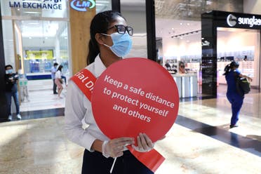 A woman wearing a protective face mask and gloves holds a sign at Mall of the Emirates after the UAE government eased a curfew and allowed stores to reopen, following the outbreak of the coronavirus disease (COVID-19) in Dubai, United Arab Emirates May 5, 2020. (AP)