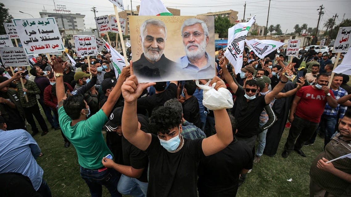 A supporter of the Iran-backed Hashed al-Shaabi (Popular Mobilization) paramilitary forces stands holding a picture showing the faces of (L to R) Qassem Soleimani and Abu Mahdi Al-Muhandes during a rally outside the entrance to Baghdad's highly-fortified Green Zone on November 7, 2020, demanding the departure of remaining US forces from Iraq. (Ahmad Al-Rubaye/AFP)