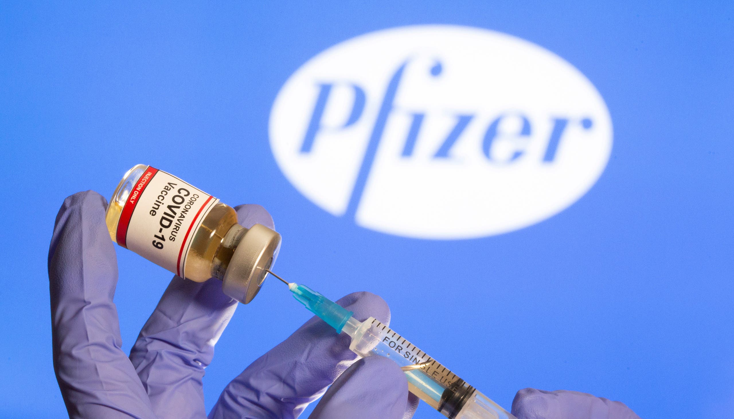 A woman holds a small bottle labeled with a Coronavirus COVID-19 Vaccine sticker and a medical syringe in front of displayed Pfizer logo in this illustration taken, October 30, 2020. (Reuters)