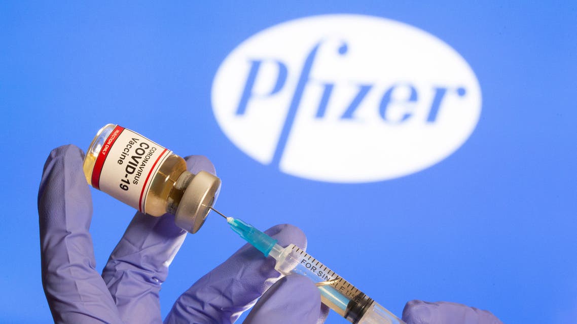 A woman holds a small bottle labeled with a Coronavirus COVID-19 Vaccine sticker and a medical syringe in front of displayed Pfizer logo in this illustration taken, October 30, 2020. (Reuters)