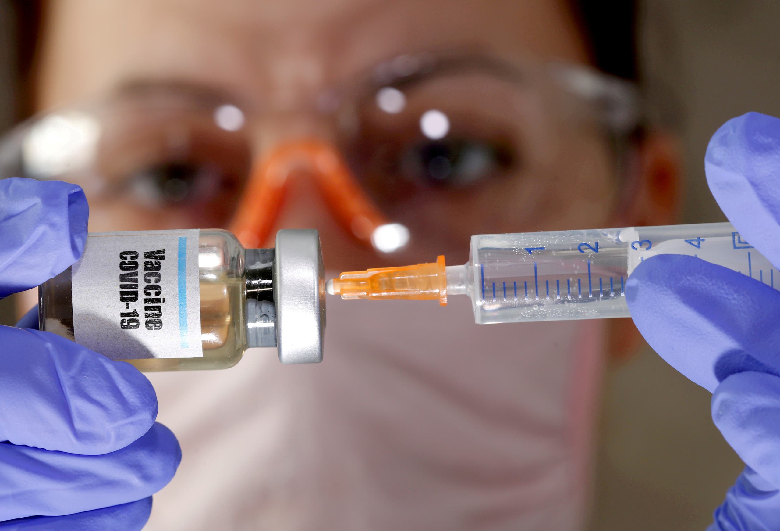 A woman holds a small bottle labeled with a Vaccine COVID-19 sticker and a medical syringe in this illustration taken April 10, 2020. (Reuters)