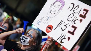 An Israeli protester wearing a protective mask due to the COVID-19 pandemic, lifts a placard as she blows a plastic horn during a demonstration against Prime Minister Benjamin Netanyahu. (AFP)