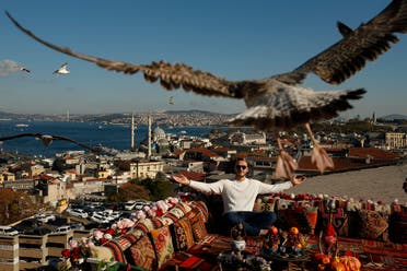 A seagull files over a man sitting at a coffee shop backdropped by the Bosporus Strait in Istanbul on Nov. 17, 2020. (AP)