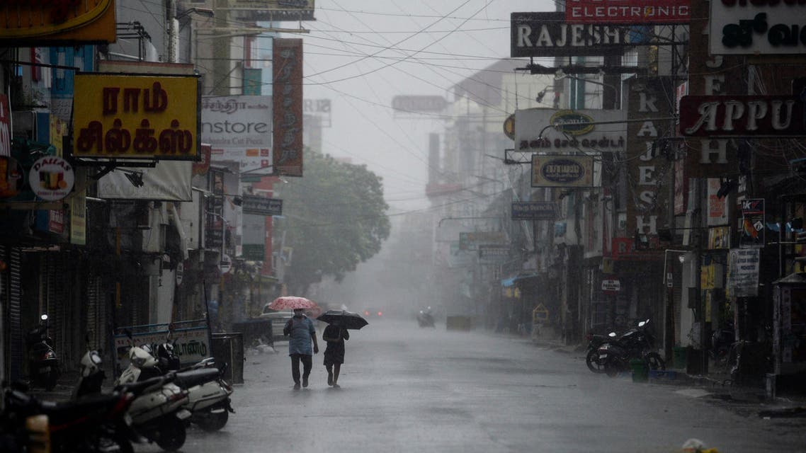 Residents shelter from heavy rain under umbrellas while walking along a deserted road as cyclone Nivar approaches the southeastern Indian coast. (AFP)