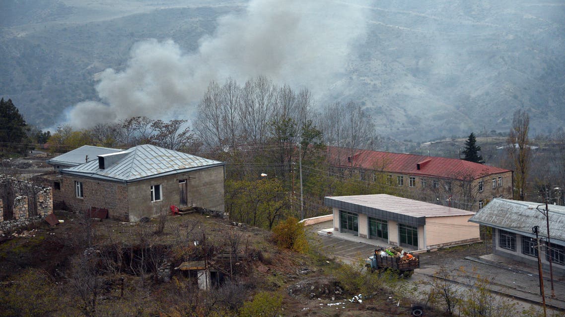 A truck loaded with firewood and other items is seen on a road in the town of Lachin (called Berdzor by the Armenians) as smoke rises from a burning house set on fire by departing residents on November 30, 2020. Armenia is to hand back the Lachin district to Azerbaijan by December 1 as part of a peace deal that ended six weeks of fighting over the breakaway region of Nagorno-Karabakh.