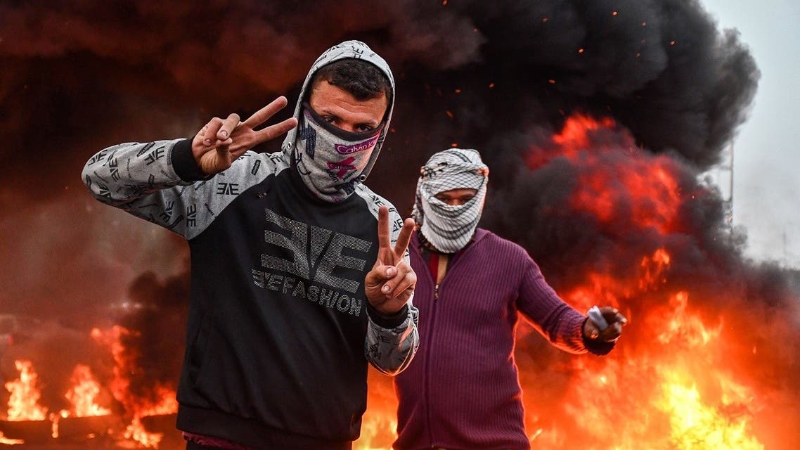 Masked protesters flash the victory gesture while standing by a fire during an anti-government demonstration in Habboubi square in the center of Iraq’s southern city of Nasiriyah in Dhi Qar province on November 29, 2020. (Asaad Niazi/AFP)
