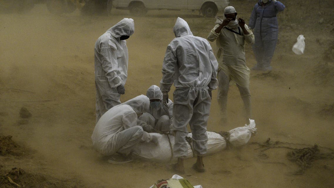 Relatives wearing protective gear tie up the dead body of a victim who died from the COVID-19 coronavirus before the burial at a graveyard in New Delhi on May 10, 2020.