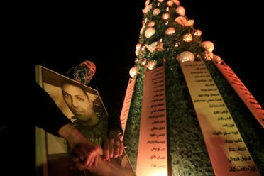 A woman holds a portrait of her relative killed during the Beirut port explosion as she passes a Christmas tree decorated with names of those who died in the Aug. 4 explosion in Beirut, Lebanon, Monday, Dec. 21, 2020. (The Associated Press)