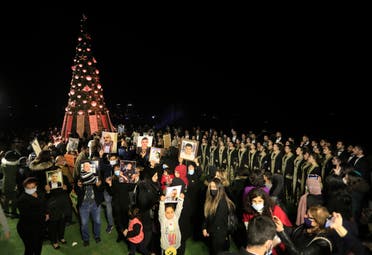 Relatives of victims killed during the Beirut port explosion hold up their portraits as they stand next to a Christmas tree decorated with names of those who died in the Aug. 4 explosion in Beirut, Lebanon, Monday, Dec. 21, 2020. (The Associated Press))