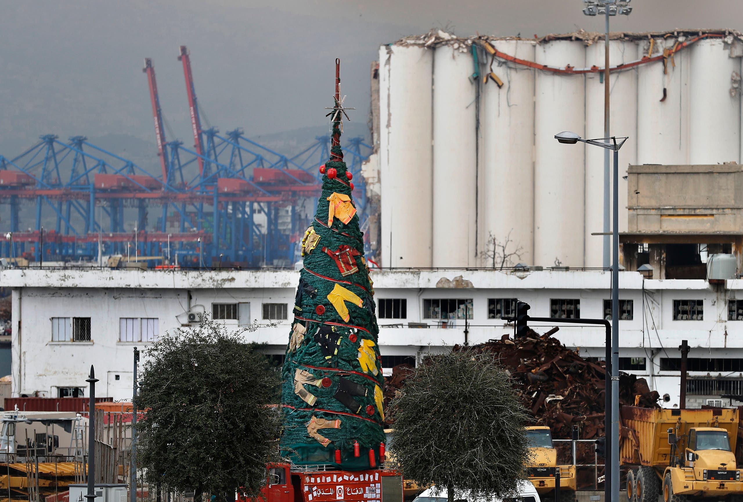 A Christmas tree decorated with firefighter uniforms to commemorate those who died while trying to extinguish the fire in the August explosion at the Beirut seaport is on display in front of damaged silos, in Beirut, Lebanon. (The Associated Press)