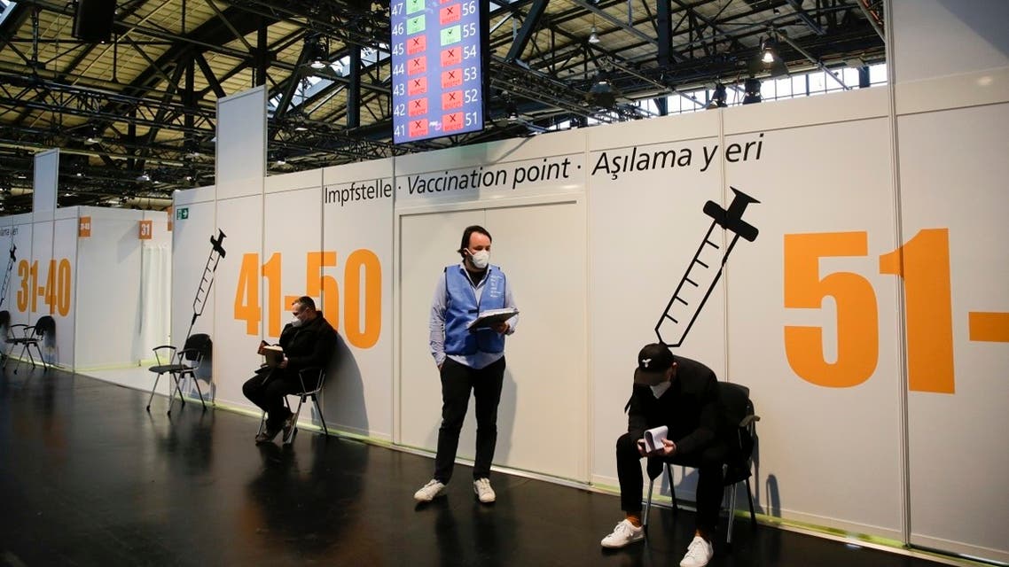 Two men sit on chairs as they wait for their vaccination at the Arena Treptow vaccine center in Berlin, on December 27, 2020, on the occasion of the Pfizer-BioNTech Covid-19 corona virus vaccine rollout. (Markus Schreiber/Pool/AFP)