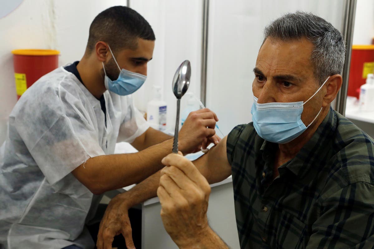 Celebrity mystic Uri Geller holds a spoon as he performs his spoon-bending trick for medical staff while receiving a vaccination against the coronavirus disease, in Jaffa, near Tel Aviv, Israel, on December 31, 2020.  (Reuters)