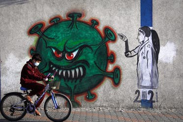 A Palestinian youth wearing a face mask rides his bicycle past a mural painting of a nurse injecting a vaccine to a COVID-19 virus in Gaza City, on December 31, 2020.  (AFP)