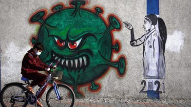 A Palestinian youth wearing a face mask rides his bicycle past a mural painting of a nurse injecting a vaccine to a COVID-19 virus in Gaza City, on December 31, 2020.  (AFP)