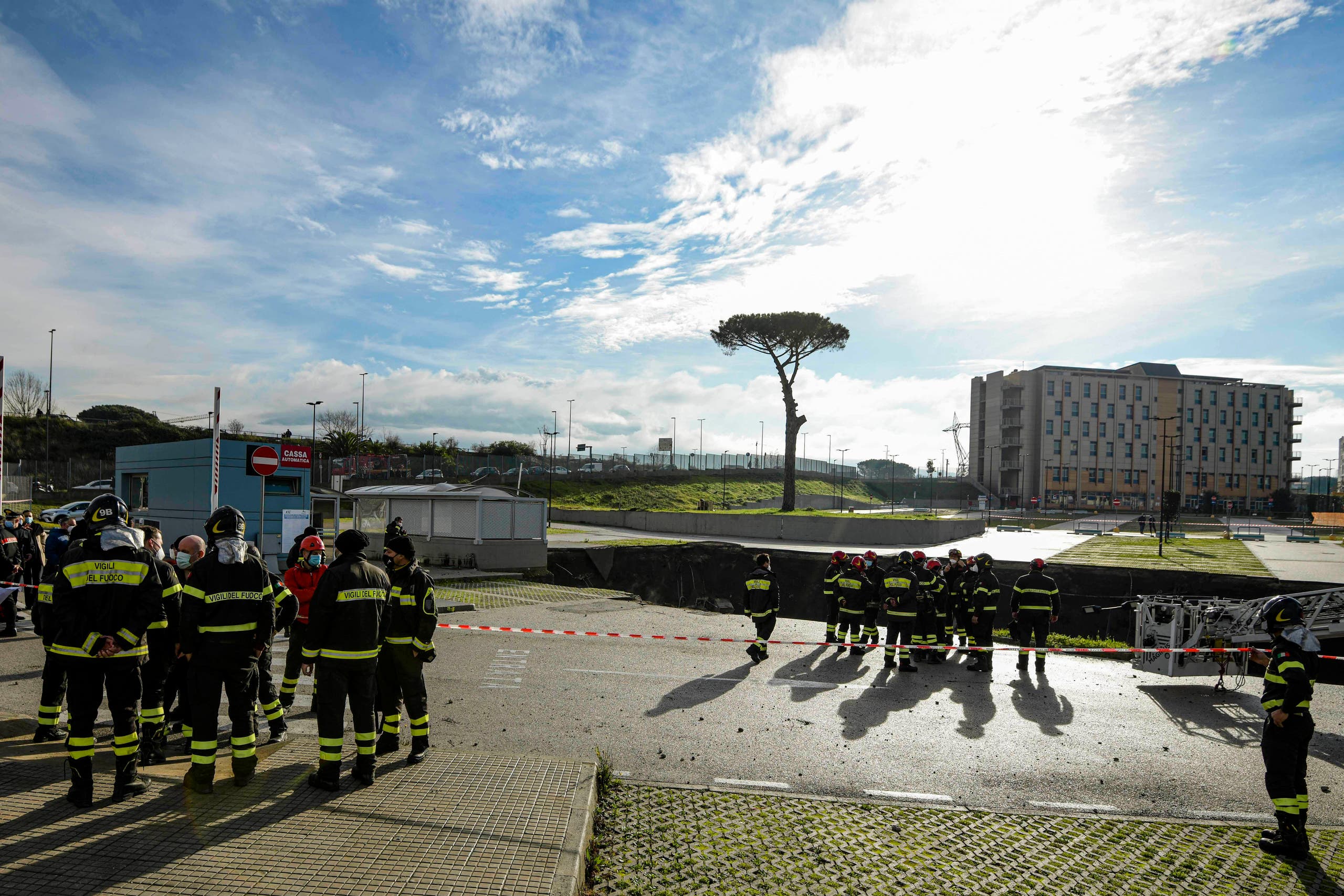 Firefighters stand on the border of the large sinkhole that opened overnight in the parking of Ospedale del Mare hospital in Naples, Italy, Friday, Jan. 8, 2021. A giant sinkhole opened Friday in the parking lot of a Naples hospital, forcing the temporary closure of a nearby residence for recovering coronavirus patients because the electricity was cut. (Alessandro Pone/LaPresse via AP)