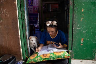 Annie Sabino, 16, a grade 9 student, completes her school work next to her dog, while tending to her family's sidewalk eatery beside their home, as schools remain closed during the coronavirus disease (COVID-19) outbreak, in Manila, Philippines. (Reuters)