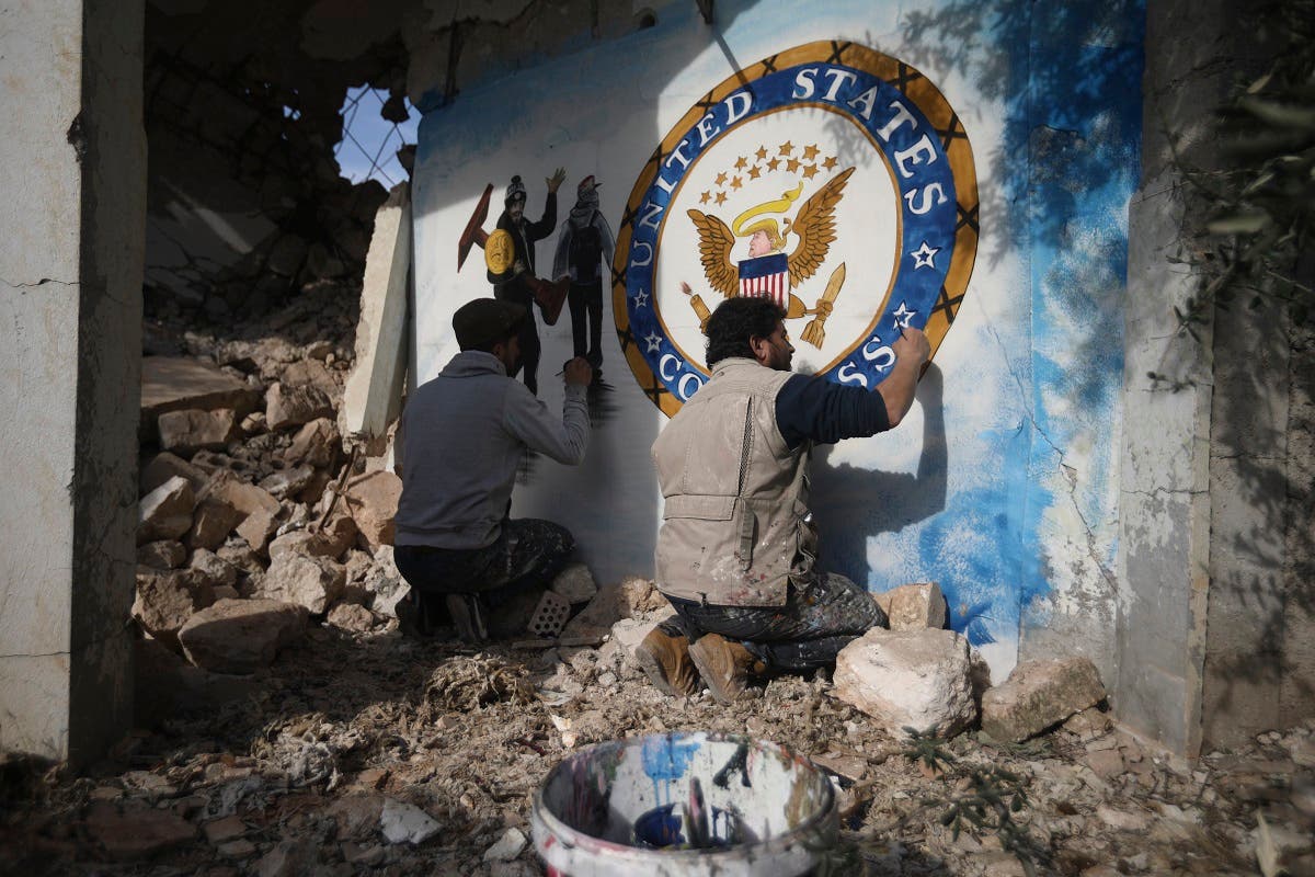 Syrian graffiti artist Aziz Al-Asmar, right, finishes work on his depiction of the events in Washington after the President Trump's supporters stormed the Capitol, on a wall of a house destroyed in an airstrike, in Binish, Idlib, Syria, Jan. 8, 2020. (AP/Ghaith Alsayed)
