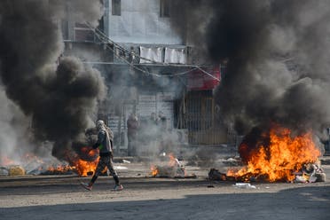 An Iraqi protester walks past burning tires during clashes with police during anti-government demonstrations in the city of Nasiriyah in the Dhi Qar province in southern Iraq on January 10, 2021. (Asaad Niazi/AFP)