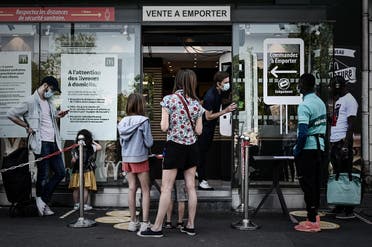 An employee of a fast food outlet talks to men working for the delivery company Deliveroo in Paris on May 27, 2020 during a partial lifting of restrictions . (AFP)