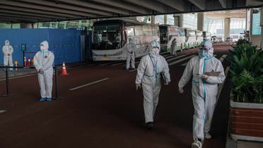 Health workers wearing a personal protection suit stands next to buses at a cordoned-off section at the international arrivals area. (AFP)