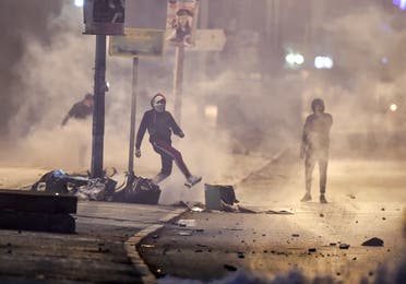 Protesters stand amidst fumes as they block a street during clashes with security forces in the Ettadhamen city suburb on the northwestwern outskirts of Tunisia's capital Tunis on January 17, 2021, amidst a wave of nightly protests in the North African country. (AFP)