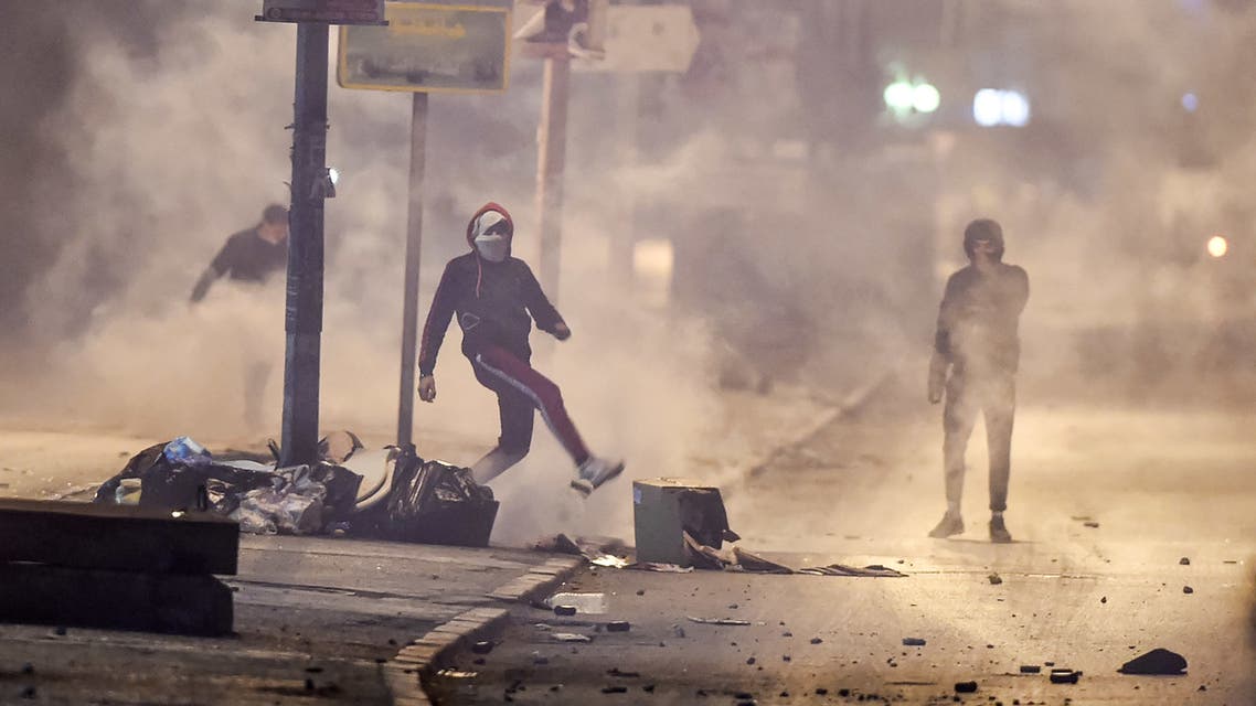 Protesters stand amidst fumes as they block a street during clashes with security forces in the Ettadhamen city suburb on the northwestwern outskirts of Tunisia's capital Tunis on January 17, 2021, amidst a wave of nightly protests in the North African country. (AFP)