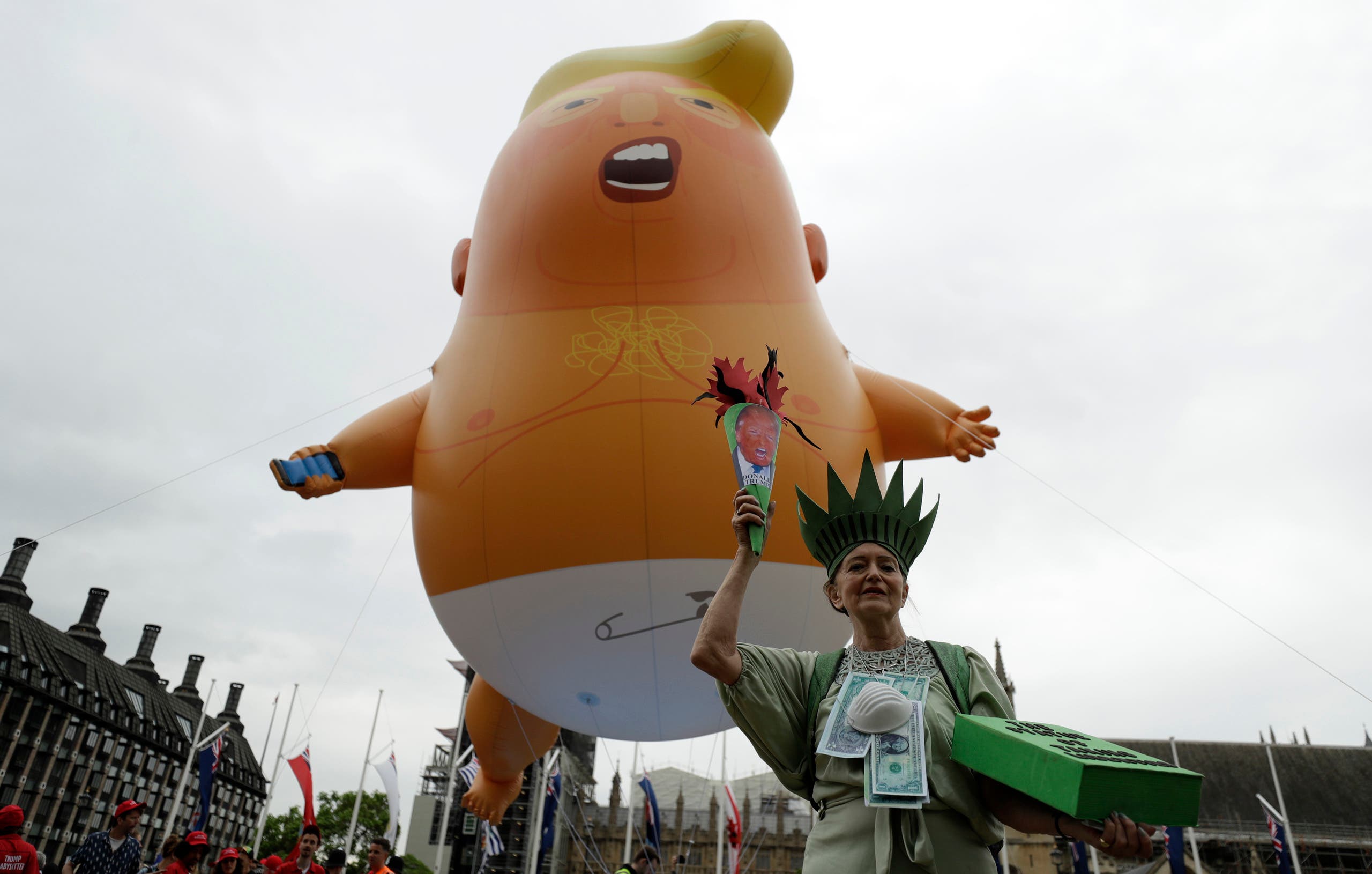 A woman posing as statue of liberty stands next to the 'Trump Baby' blimp as people gather to demonstrate against the state visit of President Donald Trump in Parliament Square, central London, Tuesday, June 4, 2019. (AP)