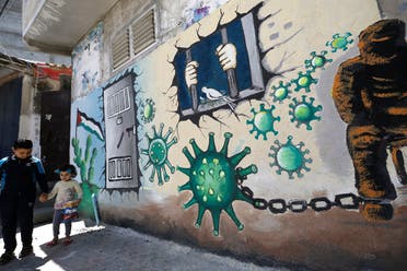 Palestinian children walk past a mural depicting the coronavirus and a prison cell, in Gaza City during the coronavirus pandemic on April 28, 2020. (Mohammed Abed/AFP)