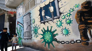 Palestinian children walk past a mural depicting the coronavirus and a prison cell, in Gaza City during the coronavirus pandemic on April 28, 2020. (Mohammed Abed/AFP)