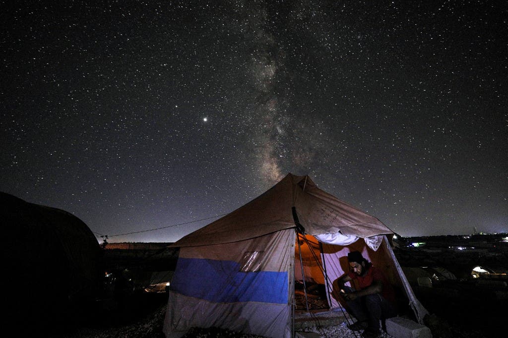 This long-exposure picture taken early on July 20, 2020, shows a man browsing a phone while seated at the entrance of a tent as the Milky Way galaxy rises in the sky above the Ahl al-Tah camp for displaced persons near the town of Maaret Misrin in Syria's northwestern Idlib province. (AFP)
