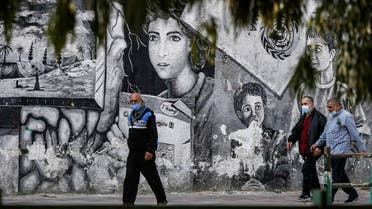 Palestinians, mask-clad due to the COVID-19 coronavirus pandemic, walk past a mural about Palestinian refugees drawn on a wall along a street in Gaza City on November 8, 2020. (Mohammed Abed/AFP)