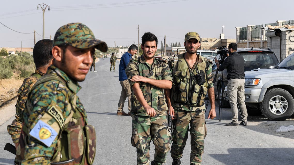 A fighter (L) wearing a military uniform bearing the insignia of the Manbij Military Council (MMC), affiliated with the Syrian Democratic Forces (SDF) Kurdish-led alliance, stands by as Syrian government soldiers walk past at a position on the outskirts of the northern city of Manbij in the north of Aleppo province, as government forces deploy there on October 15, 2019.