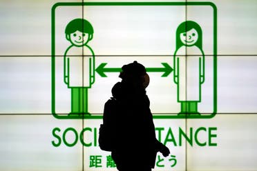 A woman wearing a protective mask to help curb the spread of the coronavirus walks in front of social distancing notice in Tokyo Tuesday, Jan. 19, 2021. (AP)