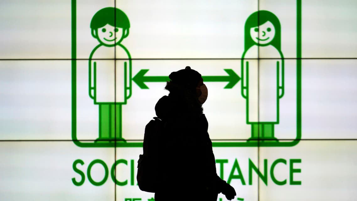 A woman wearing a protective mask to help curb the spread of the coronavirus walks in front of social distancing notice in Tokyo Tuesday, Jan. 19, 2021. (AP)