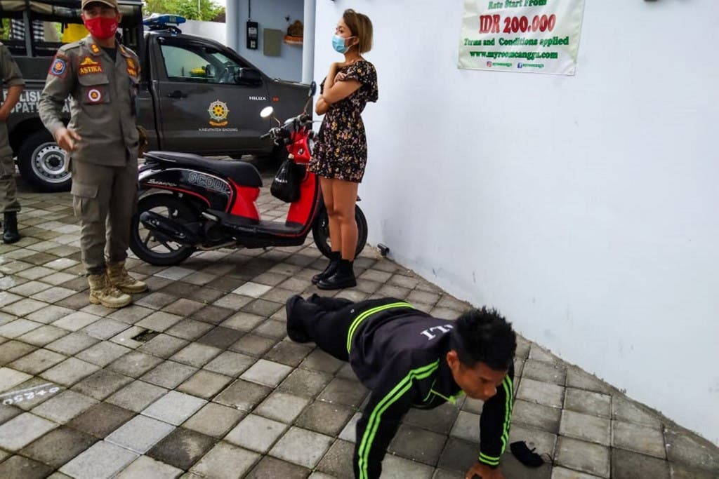 An undated handout picture released on January 20, 2021 by Bali's provincial public order agency shows an official looking on while a man performs push-ups as punishment for not wearing or improperly wearing face masks in Bali. (AFP)
