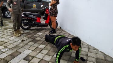 An undated handout picture released on January 20, 2021 by Bali's provincial public order agency shows an official looking on while a man performs push-ups as punishment for not wearing or improperly wearing face masks in Bali. (AFP)