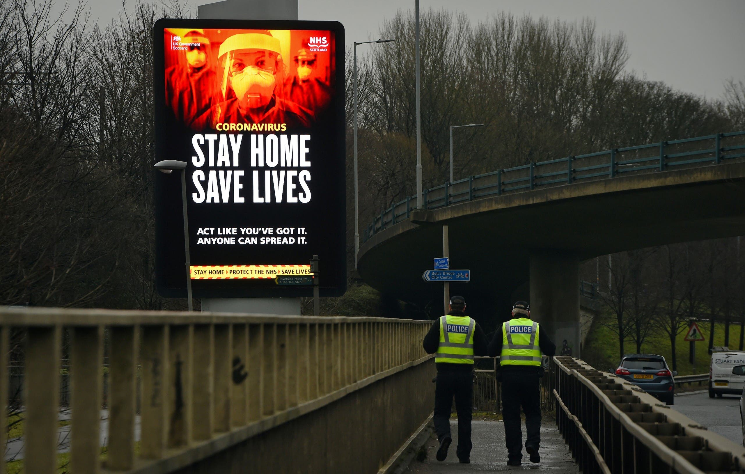 Police officers walk past a COVID-19 information board alongside the Clydeside Expressway in Glasgow, UK. (AFP)