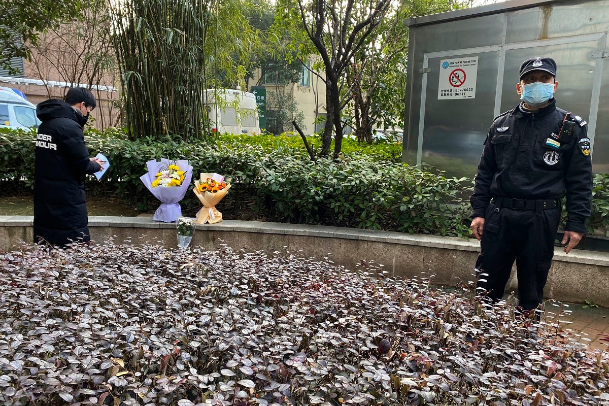 A security guard stands nearby as a man visiting the Wuhan Central Hospital leaves flowers in memory of Li Wenliang, Feb. 7, 2021. (AP/Ng Han Guan)