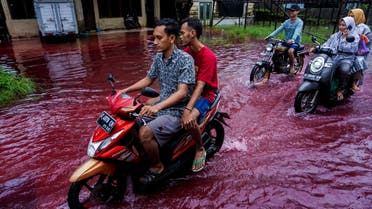 People ride motorbikes through a flooded road with red water due to the dye-waste from cloth factories, in Pekalongan, Central Java province, Indonesia, February 6, 2021. (Reuters)