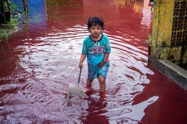A girl walks through a flooded road with red water due to the dye-waste from cloth factories, in Pekalongan, Central Java province, Indonesia, February 6, 2021. (Reuters)