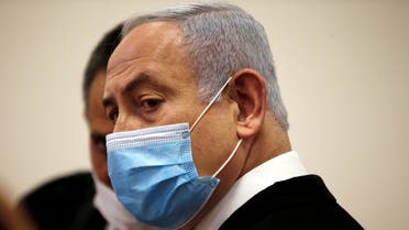 Israeli Prime Minister Benjamin Netanyahu, wearing a face mask, looks on while standing inside the court room as his corruption trial opens at the Jerusalem District Court. (Reuters)