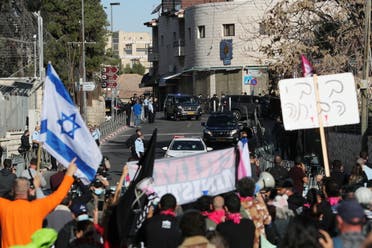 Protesters hold placards and an Israeli flag as a convoy transporting Israeli Prime Minister Benjamin Netanyahu to the District Court arrives ahead of a hearing in his corruption trial in Jerusalem. (Reuters)