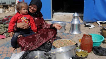 An internally displaced woman with a child on her lap prepares food outside a tent in Azaz, Syria February 28, 2020. REUTERS/Khalil Ashawi