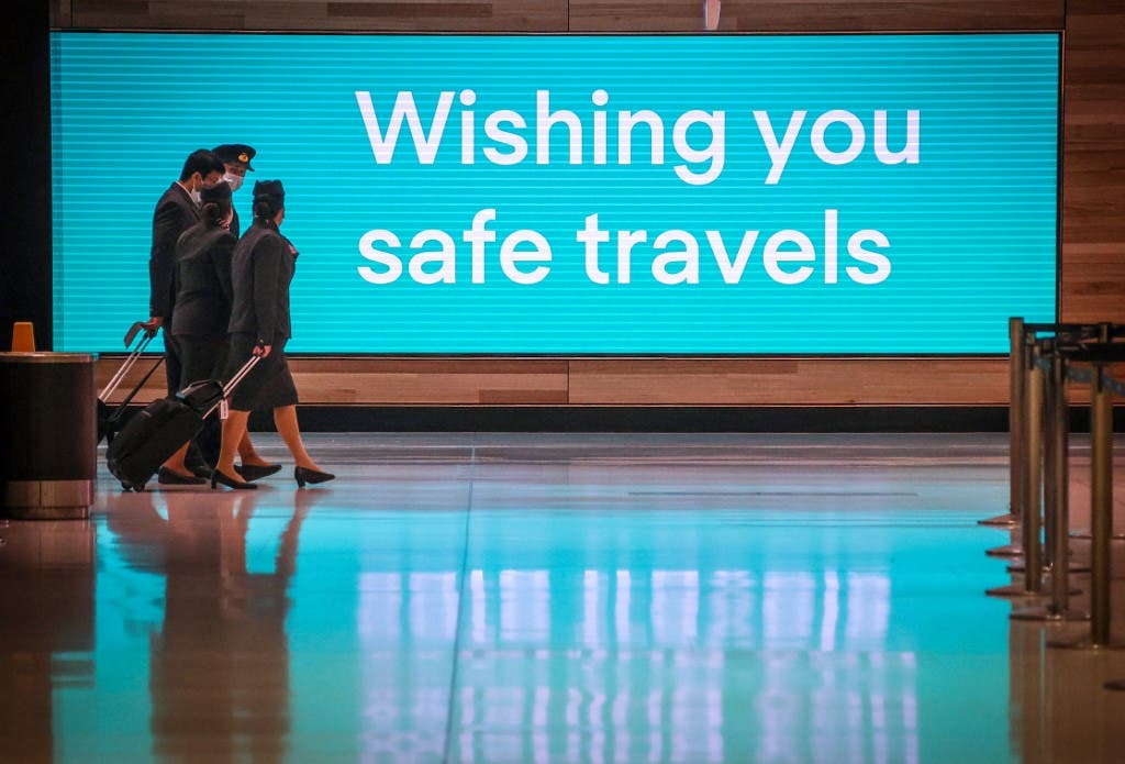 Flight crew members wearing face masks as a preventive measure against the COVID-19 novel coronavirus as they walk past an illuminated sign in the Sydney International Airport in Sydney. (File photo: AFP)
