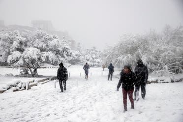 People make their way as the Parthenon temple is seen atop the Acropolis hill archaeological site during a heavy snowfall in Athens, Greece, on February 16, 2021. (Reuters)