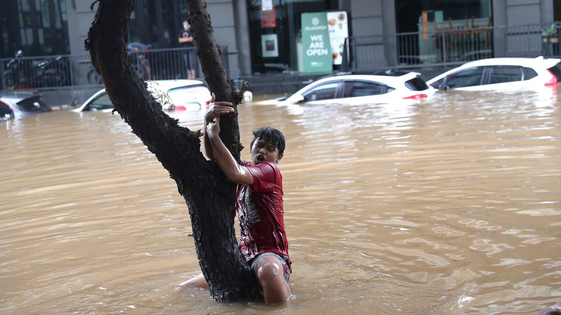 A man grabs a tree to keep from being swept away by flood water through a flooded neighborhood following heavy rains in Jakarta, Indonesia, Saturday, February 20, 2021. (AP)
