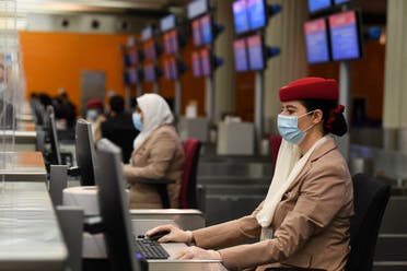 Ground hostesses of the Emirates airlines wear face masks and assist travellers fromp behind glass windows at Dubai International Airport on May 22, 2020, after the resumption of scheduled operations by the Emirati carrier, amid the ongoing novel coronavirus pandemic crisis. (AFP)