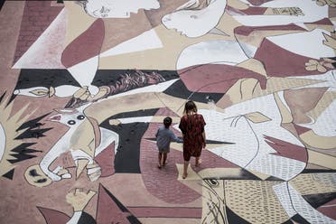 A mother and child walk on a giant reproduction in sand of Spanish artist Pablo Picasso's Guernica painting, during Taiwanese-American artist Lee Mingwei's performance Guernica in Sand part of his Gifts and Rituals exhibition at the Martin-Gropius-Bau museum in Berlin on July 4, 2020.  (AFP)
