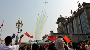 People hold their mobile phones and Chinese flags as military aircraft fly in formation during the military parade marking the 70th founding anniversary of People’s Republic of China, at a railway station in Beijing, China, on October 1, 2019. (Reuters)